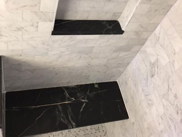 Dark Vermont Soapstone accents for the seat and inset shelves create the perfect accent to this marble shower surround.